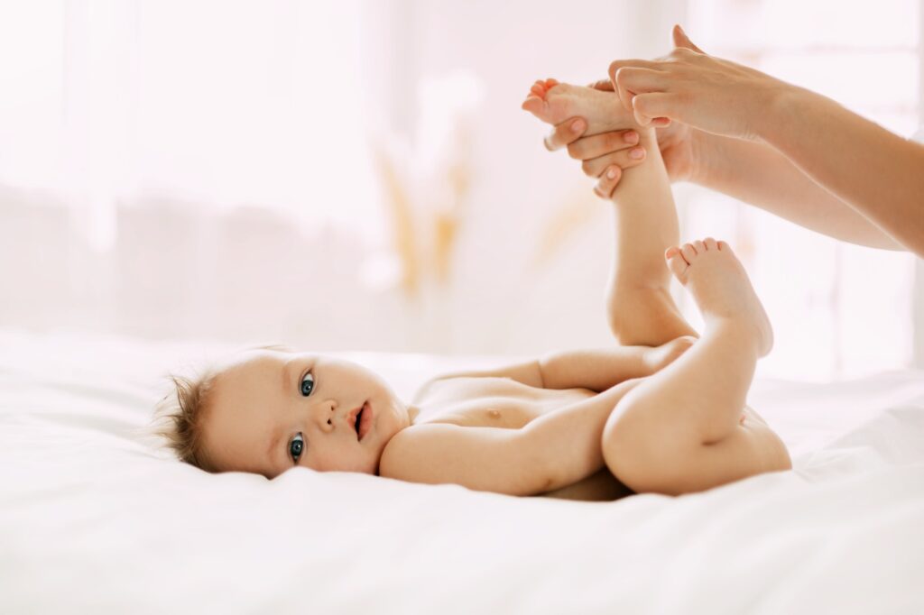 A young mother gently massages her child's legs. Child care, childhood, motherhood.